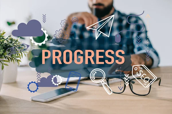 Cropped shot of businessman in plaid shirt sitting at workplace with progress icons — Stock Photo