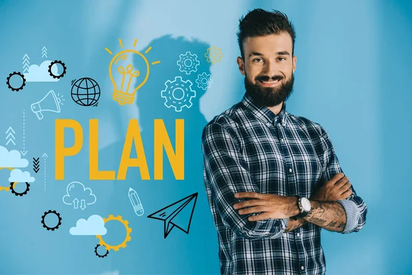 Bearded smiling businessman posing with crossed arms, on blue with plan icons — Stock Photo