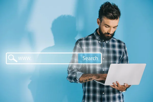 Бородатий розробник використовує ноутбук, на синьому з панеллю пошуку веб-сайту — стокове фото