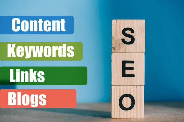 SEO word made from wooden blocks on blue background with Content, Keywords, Links, Blogs signs — Stock Photo