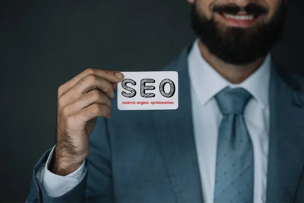 Cropped view of smiling developer and showing business card with SEO sign — Stock Photo