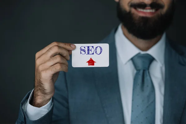 Cropped view of successful developer smiling and showing business card with SEO sign — Stock Photo