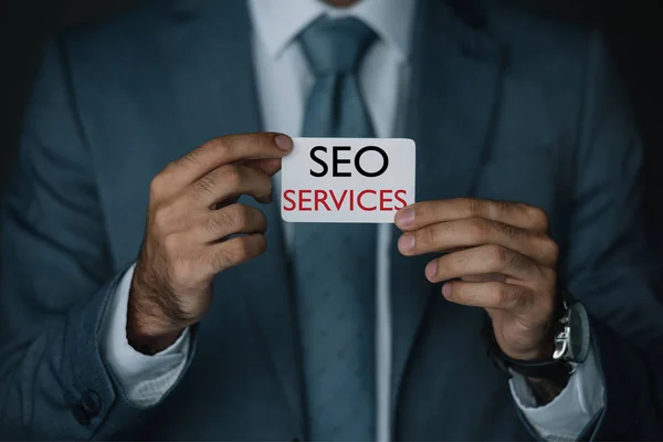 Vista recortada del desarrollador en traje con tarjeta de visita con servicios SEO - foto de stock