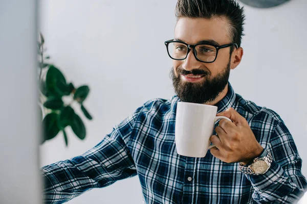 Schnappschuss eines glücklichen jungen SEO mit einer Tasse Kaffee bei der Arbeit mit dem Computer im Büro — Stockfoto