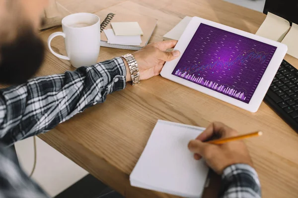 Cropped shot of seo using tablet with statistics chart on screen and writing notes at workplace — Stock Photo