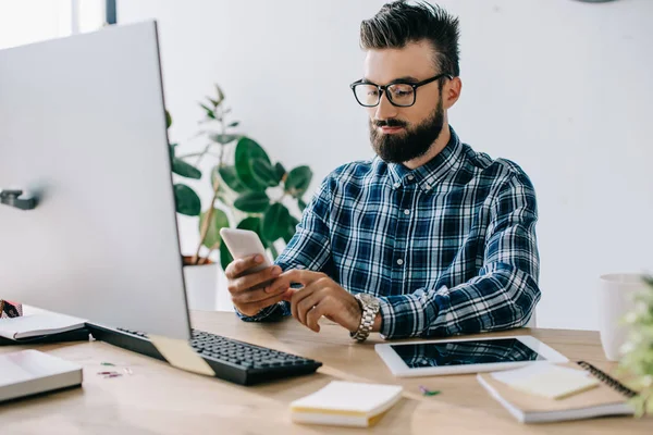 Handsome bearded young businessman using smartphone at workplace — Stock Photo