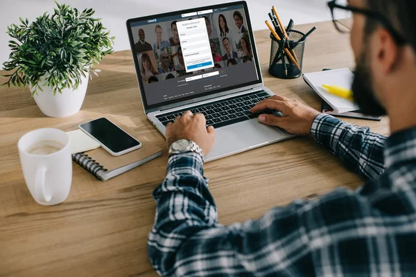 Cropped shot of man in plaid shirt using laptop with linkedin website on screen — Stock Photo