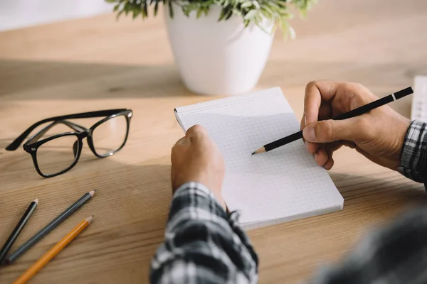 Cropped shot of man writing in notebook at workplace — Stock Photo