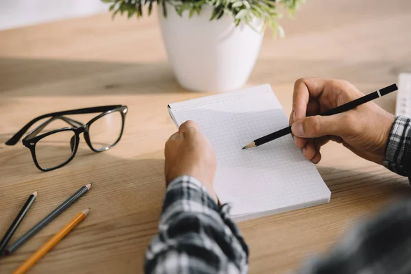 Tiro recortado do homem que escreve no caderno no local de trabalho — Fotografia de Stock