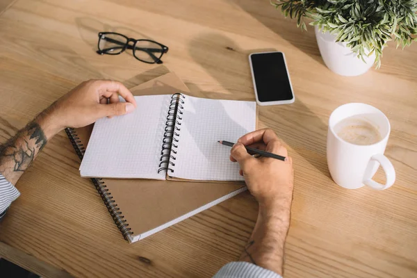 Tiro recortado do homem que escreve no caderno no local de trabalho — Fotografia de Stock