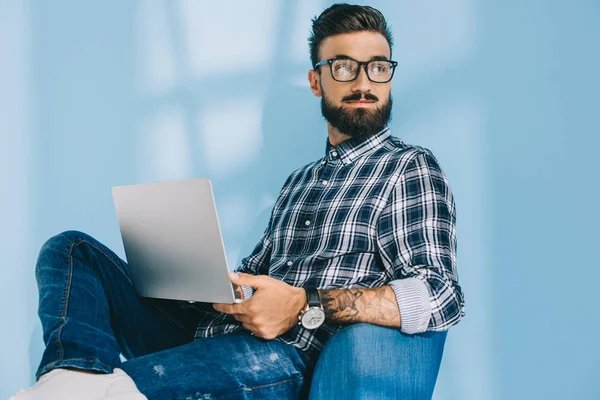 Homem bonito em camisa quadriculada usando laptop e sentado em poltrona — Fotografia de Stock