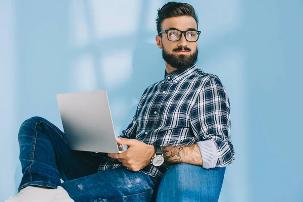 Bell'uomo in camicia a scacchi con computer portatile e seduto in poltrona — Foto stock