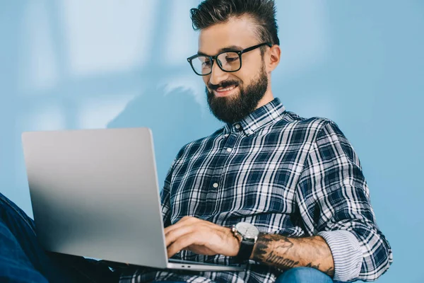 Hombre sonriente guapo usando el ordenador portátil, en azul - foto de stock