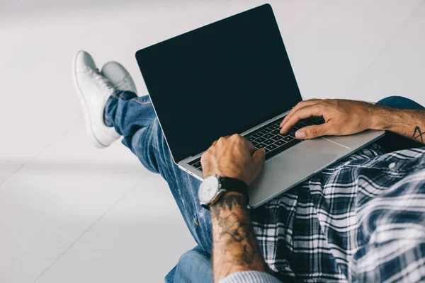 Vista recortada del hombre tatuado escribiendo en el ordenador portátil con pantalla en blanco - foto de stock