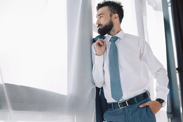 Hombre de negocios barbudo mirando a la ventana en la oficina - foto de stock