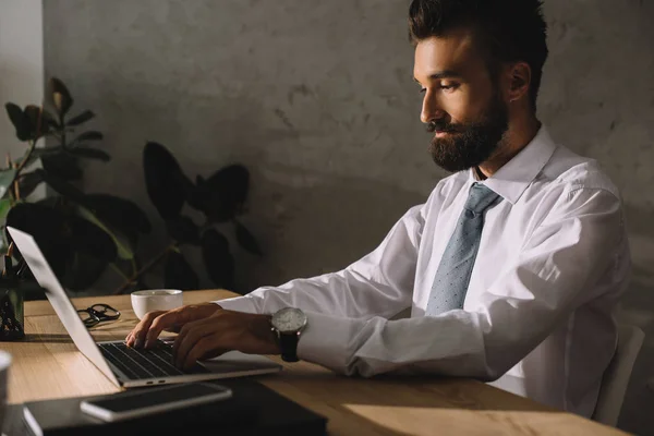 Красивый бородатый бизнесмен с ноутбуком в офисе — стоковое фото