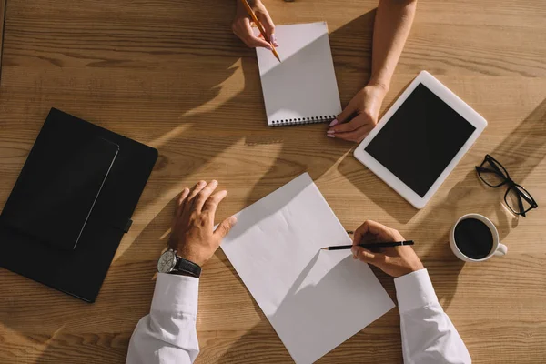 Top view of businesspeople working and writing at wooden table with coffee and digital tablet — Stock Photo