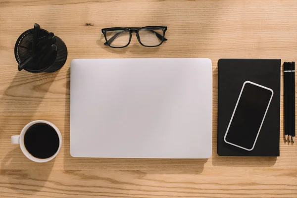 Вид зверху офісного приладдя, ноутбук, смартфон, окуляри та чашка кави — стокове фото