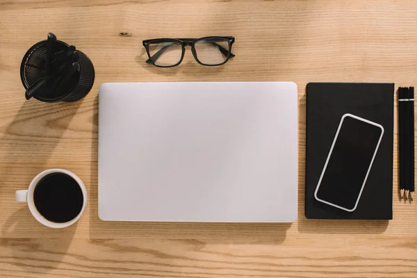 Vista dall'alto di forniture per ufficio, laptop, smartphone, occhiali e tazzina da caffè — Foto stock