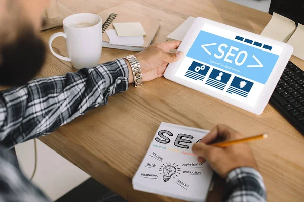 Cropped shot of seo manager using tablet and writing notes at workplace — Stock Photo