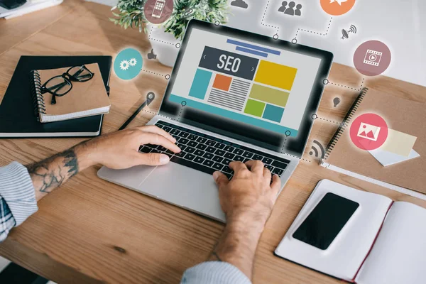 Cropped shot of developer using laptop with SEO icons at workplace — Stock Photo