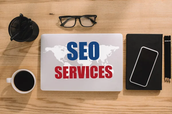 Vue d'ensemble des services SEO et carte du monde sur ordinateur portable avec fournitures de bureau autour — Photo de stock