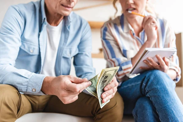 Cropped shot of elderly couple counting money and taking notes during relocation — Stock Photo