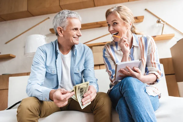 Feliz pareja de ancianos contando dinero y riendo mientras se muda a casa - foto de stock