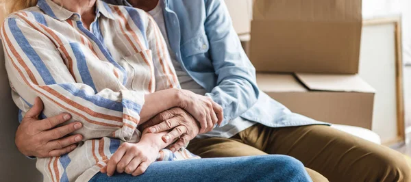 Partial view of senior couple holding hands and sitting together on couch in new house — Stock Photo