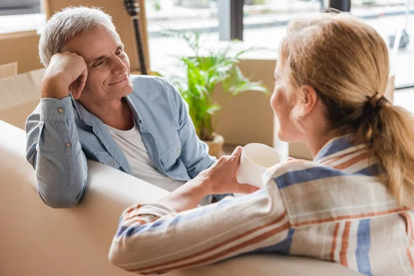 Feliz pareja de ancianos sentados en el sofá y sonriendo el uno al otro mientras se trasladan a casa nueva - foto de stock