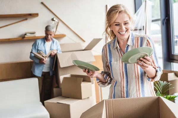 Smiling woman packing plates and husband standing behind during relocation — Stock Photo