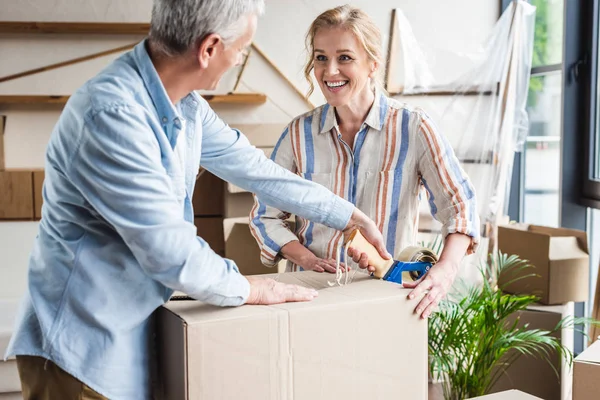 Happy senior couple packing cardboard box and smiling each other during relocation — Stock Photo