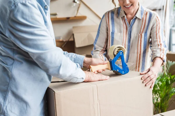 Обрезанный снимок улыбающейся пожилой пары, упаковывающей картонную коробку во время переезда — стоковое фото