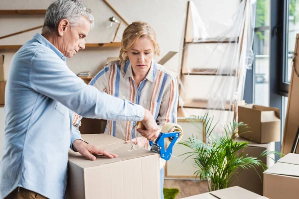 Focused senior couple packing cardboard boxes while moving home — Stock Photo