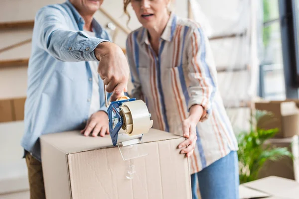 Cropped shot of senior couple packing cardboard box during relocation — Stock Photo