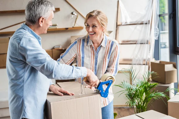 Happy elderly couple packing cardboard boxes during relocation — Stock Photo