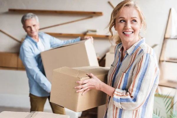 Happy elderly couple holding cardboard boxes while moving home — Stock Photo