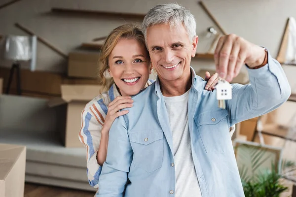 Feliz casal de idosos segurando chaves da nova casa e sorrindo para a câmera — Fotografia de Stock
