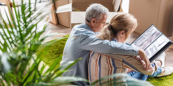 Vue grand angle du couple de personnes âgées regardant l'album photo lors de la réinstallation dans une nouvelle maison — Photo de stock