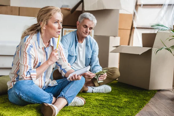 Senior couple sitting on carpet and counting money during relocation — Stock Photo