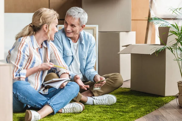 Happy senior couple sitting on carpet and counting money during relocation — Stock Photo