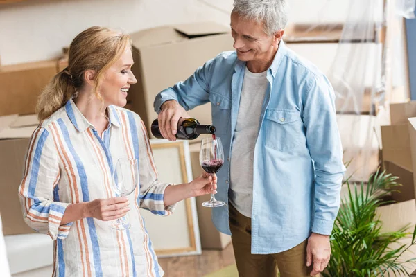 Homme âgé heureux versant du vin à sa femme tout en célébrant la réinstallation — Photo de stock