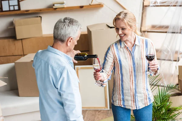 Seniorchef schenkt glücklicher Frau Wein ein, während sie Umzug im neuen Haus feiert — Stockfoto