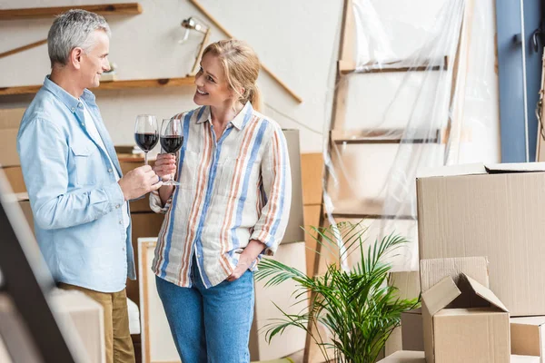 Happy elderly couple holding glasses of wine and smiling each other during relocation — Stock Photo