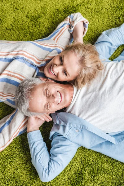 Vista superior de feliz pareja de ancianos acostados juntos en la alfombra verde - foto de stock