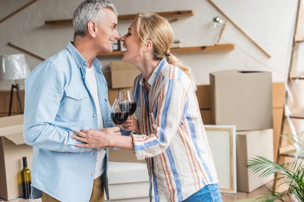 Vue latérale du couple heureux de personnes âgées buvant du vin lors de la réinstallation dans une nouvelle maison — Photo de stock