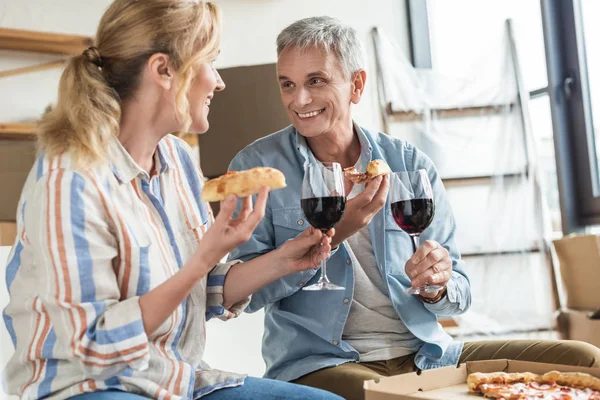 Feliz pareja de ancianos comiendo pizza y bebiendo vino en casa nueva - foto de stock