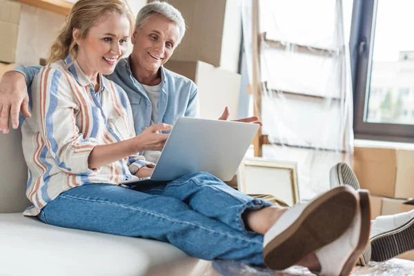 Feliz pareja de ancianos sentado y el uso de la computadora portátil durante la reubicación en casa nueva - foto de stock