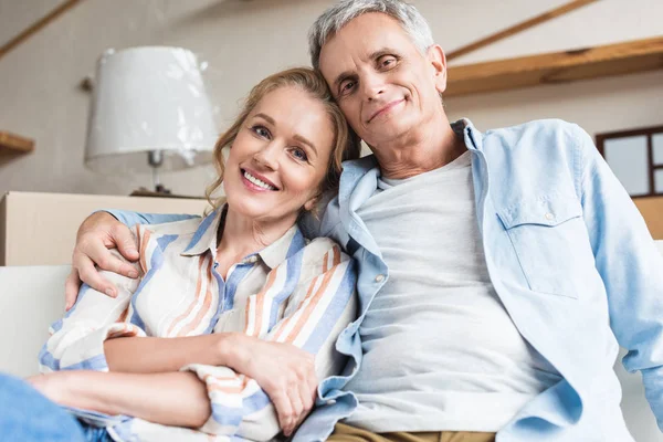 Heureux couple aîné embrasser et sourire à la caméra dans la nouvelle maison — Photo de stock