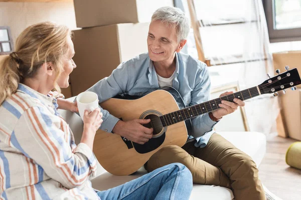 Happy grey hair man playing guitar and looking at beautiful wife during relocation — Stock Photo